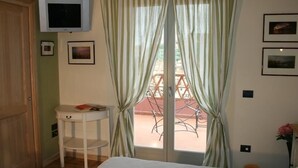 A bedroom with a bed, a small bedside table with books, a TV mounted on the wall, and a balcony with a railing. - La Terrazza di Reggello (Reggello)