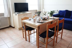 A dining area with a table set for four, a television on a cabinet, and a blue sofa in the background. - Residenza Cavour (Parma)
