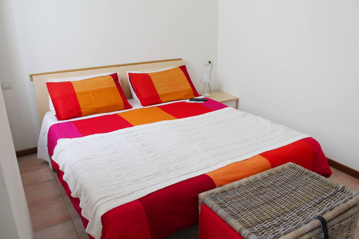 A neatly made bed with a red and white bedspread, a wooden headboard, and a small bedside table with a lamp.