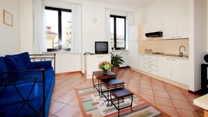 Un espacio habitable compacto con un sofá, una mesita con un florero, un televisor y una zona de cocina con armarios y un lavamanos.