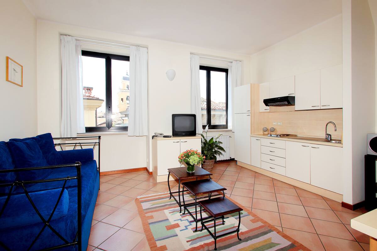 A compact living space with a sofa, a small table with a vase, a television, and a kitchen area with cabinets and a sink.