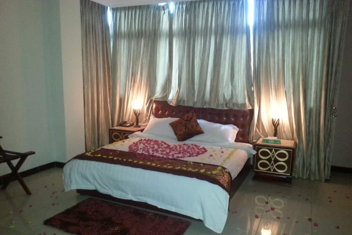 A neatly made bed with rose petals, a wooden headboard, and two bedside tables with lamps.