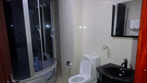 Un bagno con cabina doccia in vetro, un water bianco, un lavandino nero e uno specchio sopra il lavandino.