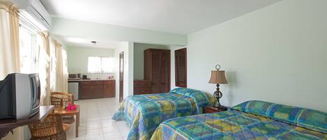 A hotel room with two beds, a TV, a desk, and a kitchenette.