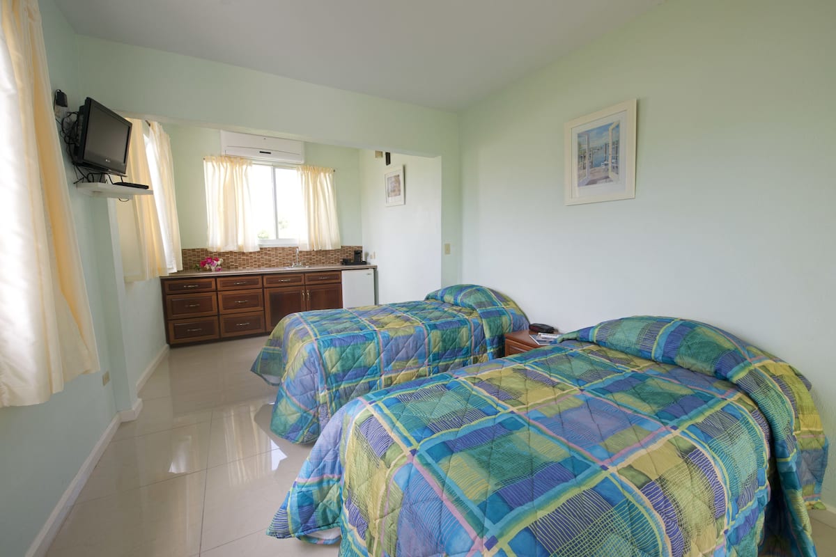 Quarto com duas camas, televisão na parede, penteadeira e janela com cortinas.