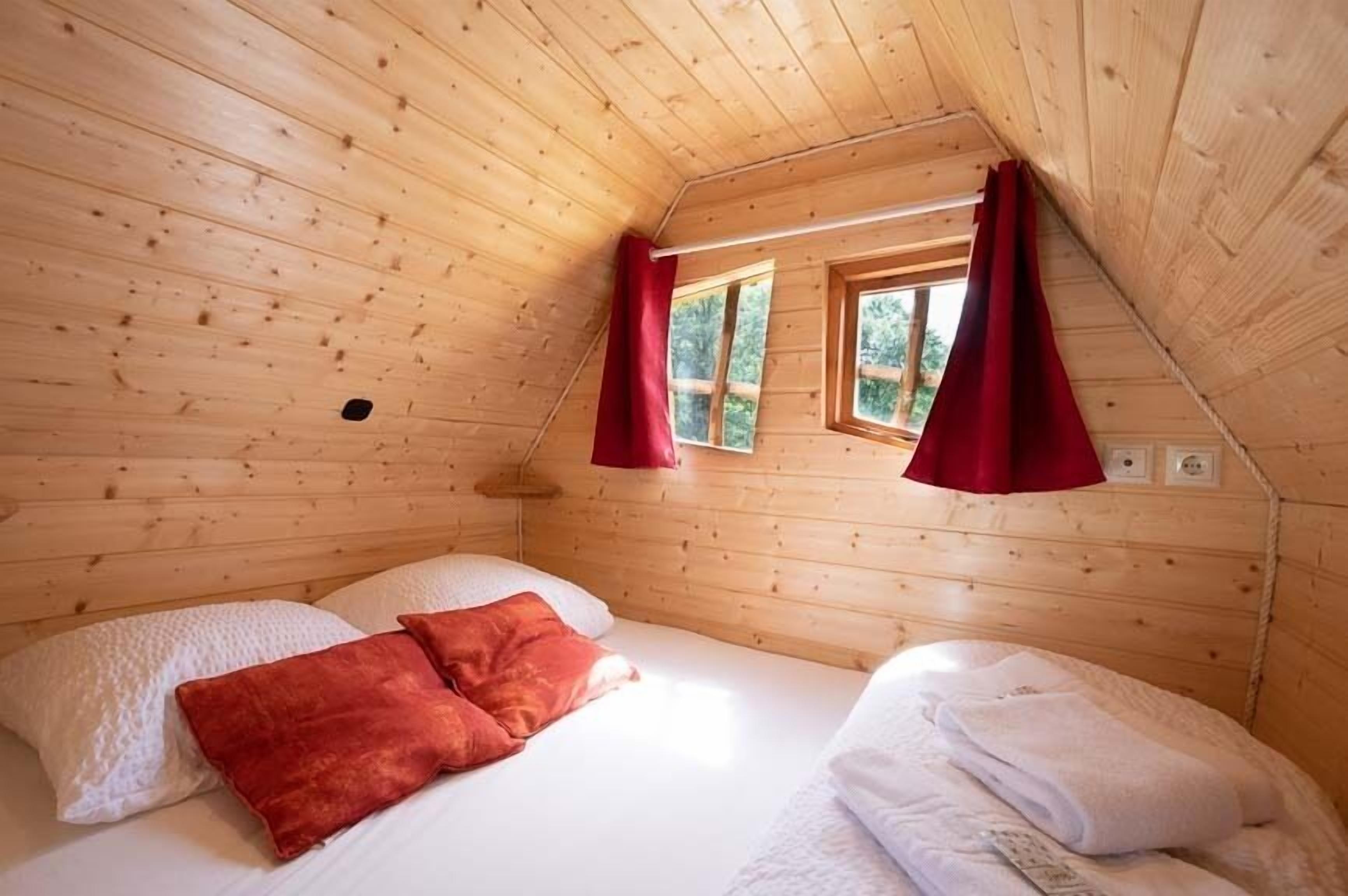 Un dormitori d'una cabana de fusta acollidora amb dos llits, cortines vermelles i una petita finestra.