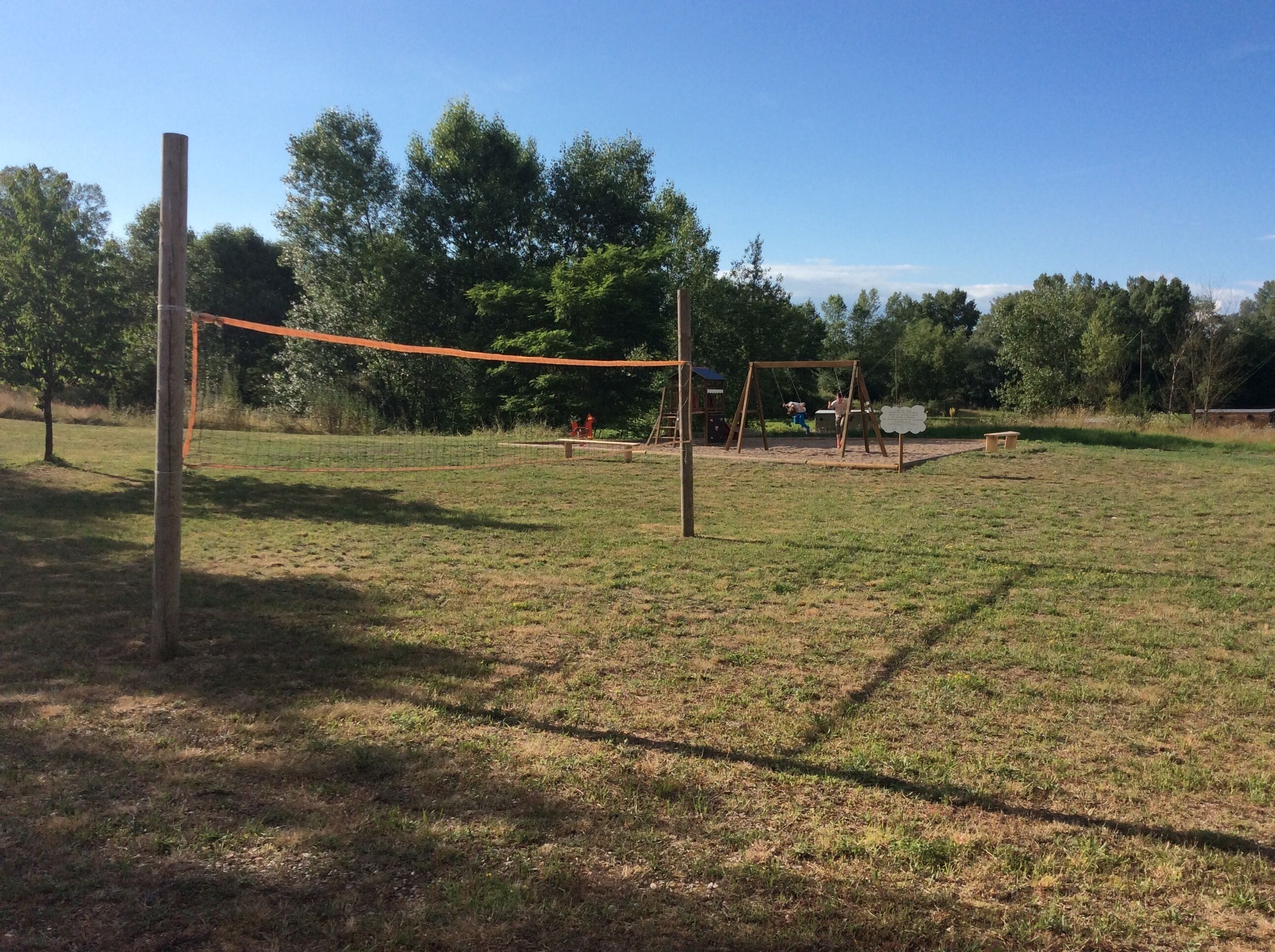 Een grasveld met een volleybalnet, een schommel en een picknicktafel.