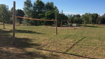 Een grasveld met een volleybalnet, een schommel en een picknicktafel.