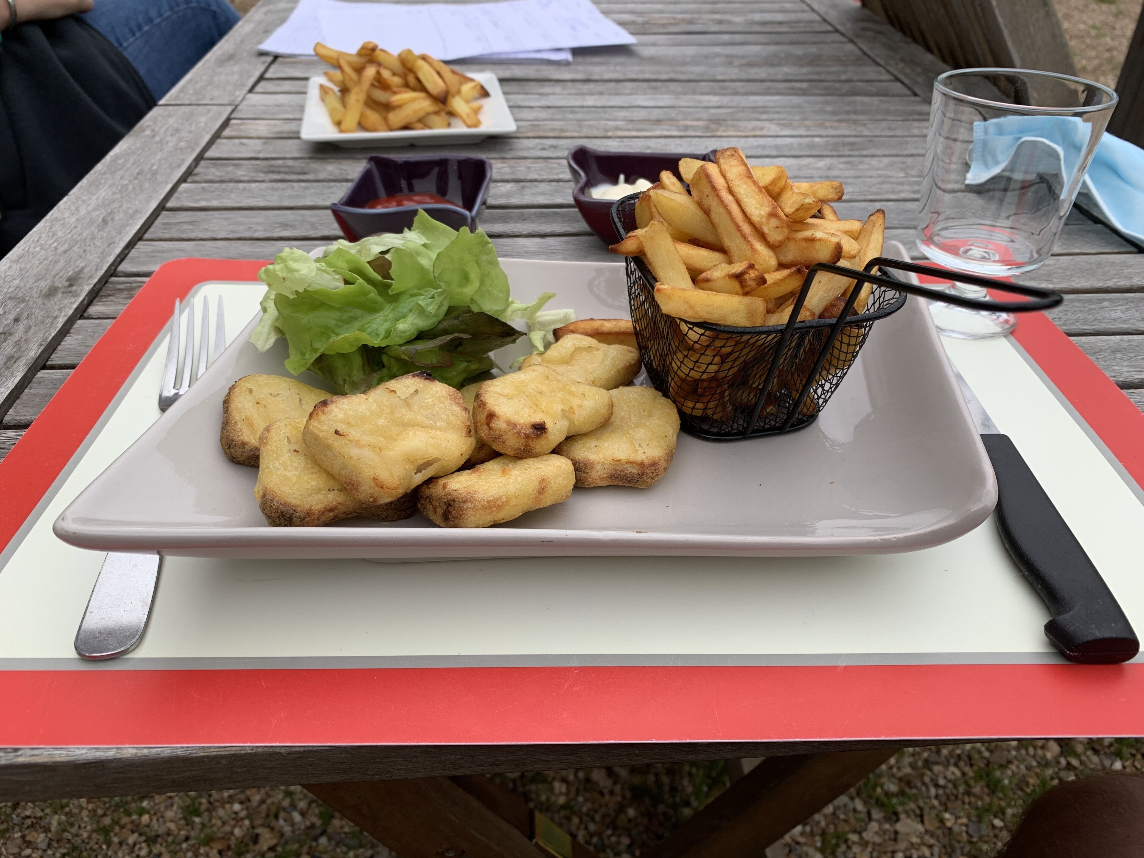 A meal of fries, chips, and lettuce on a wooden table with a red tray.