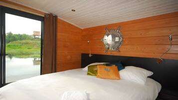 A bedroom with a large bed, wooden walls, a view of a water body, and a ship's wheel decoration.