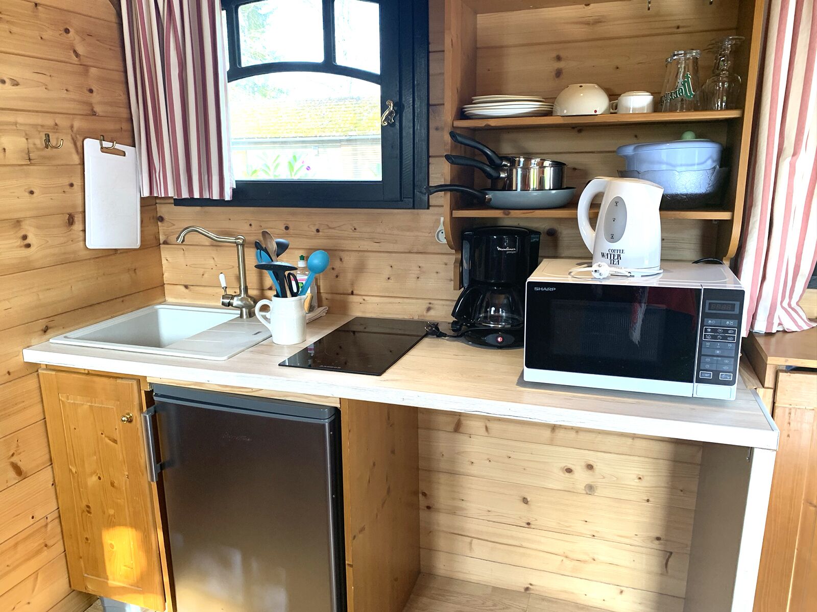 Een kleine keuken met houten wanden, een spoelbak, een magnetron, een koffiezetapparaat en verschillende keukengerei.