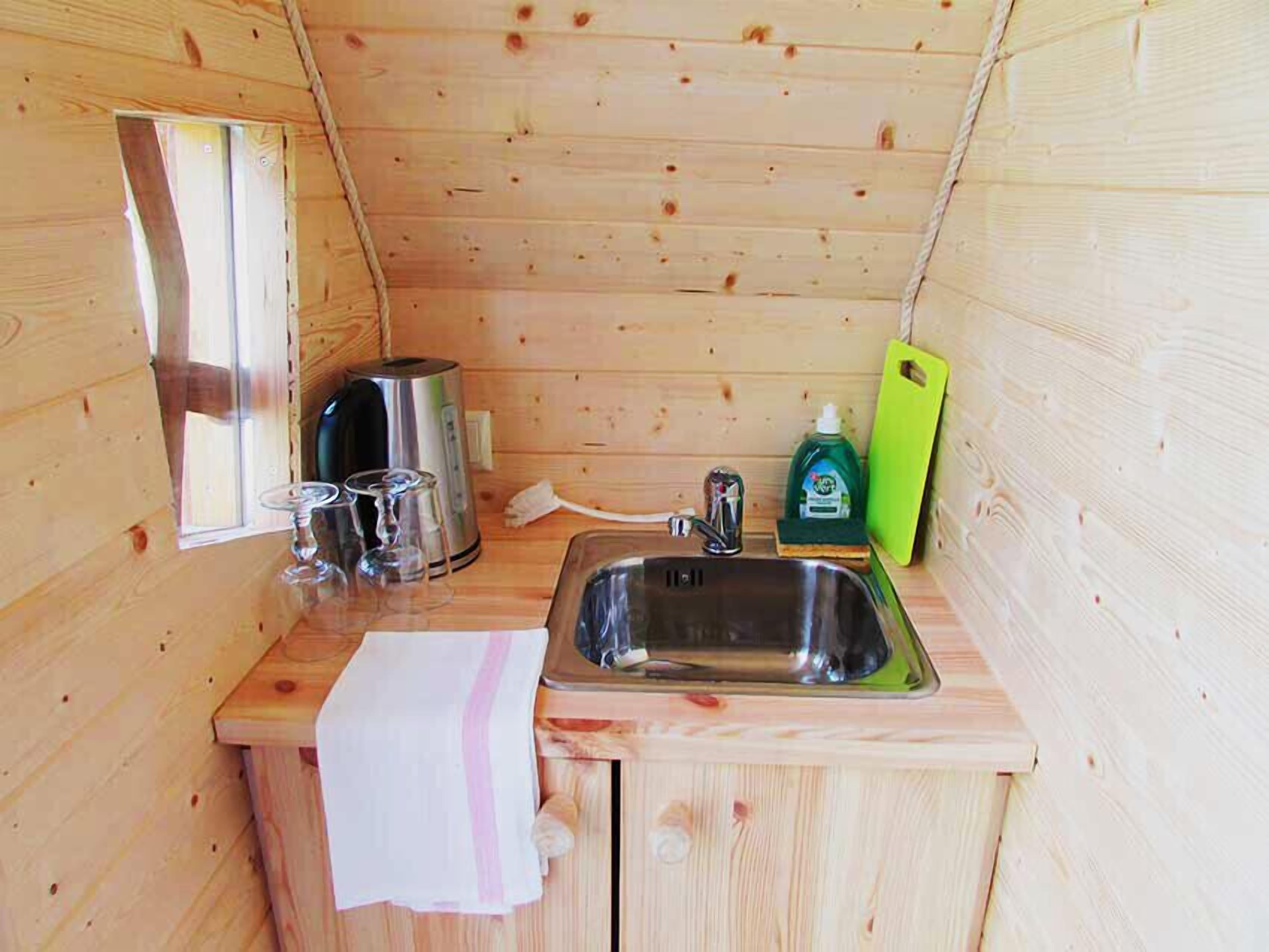 Uma cabana de madeira compacta com cozinha compacta, incluindo uma pia, chaleira e tábua de corte verde.