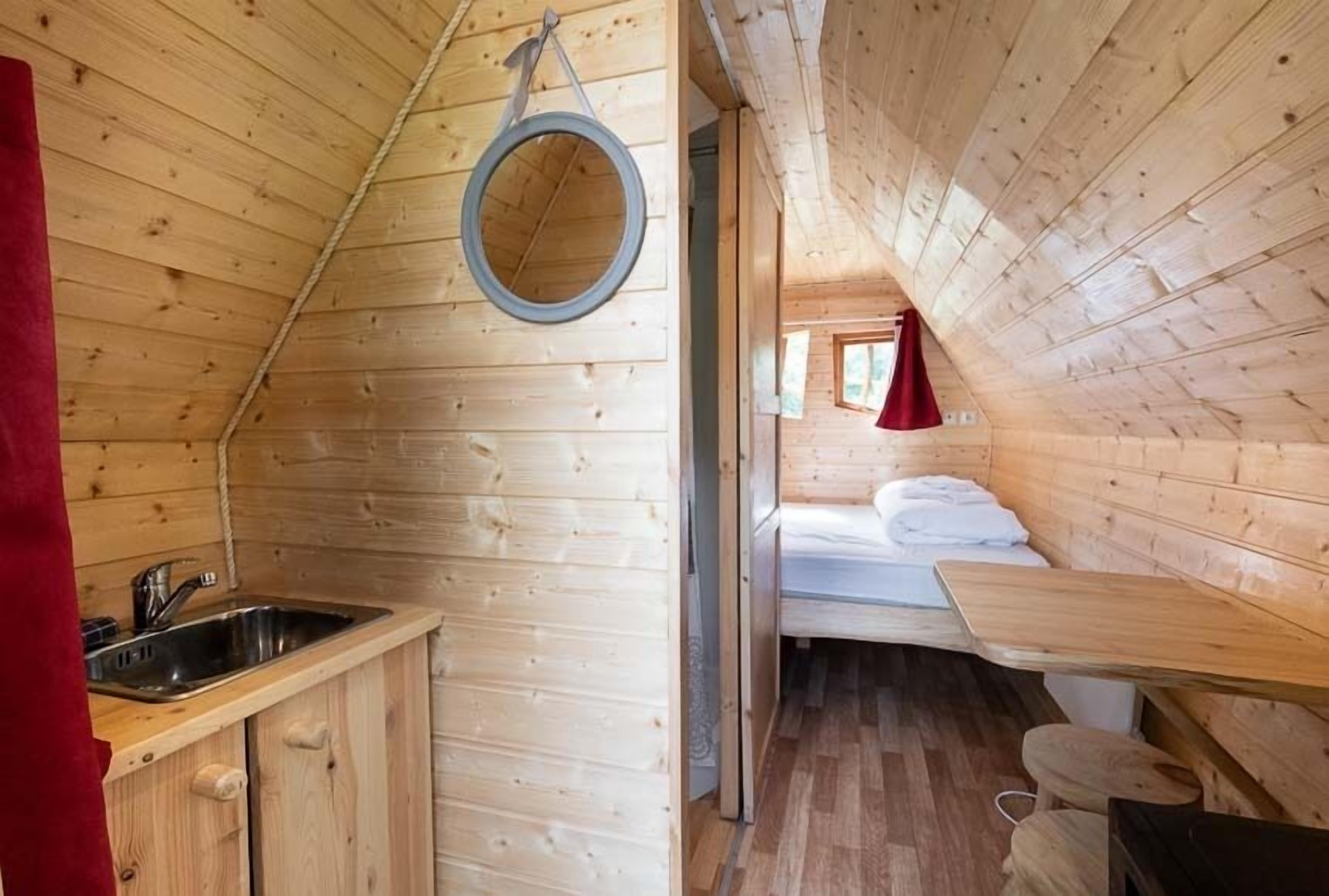 A wooden cabin interior with a kitchen area, a bed, and a small seating area.