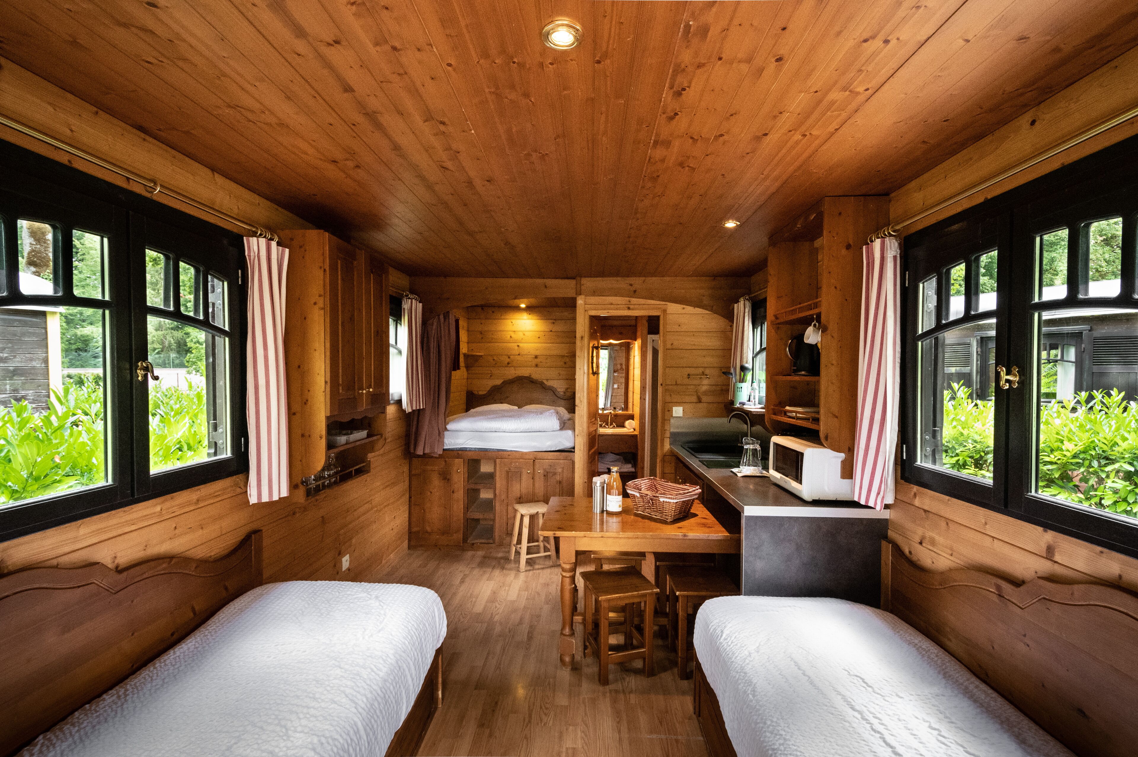 A cabin with two beds, a wooden interior, a kitchen area, and large windows.