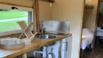 A compact kitchen with a sink, a small refrigerator, and wooden shelves with kitchenware.