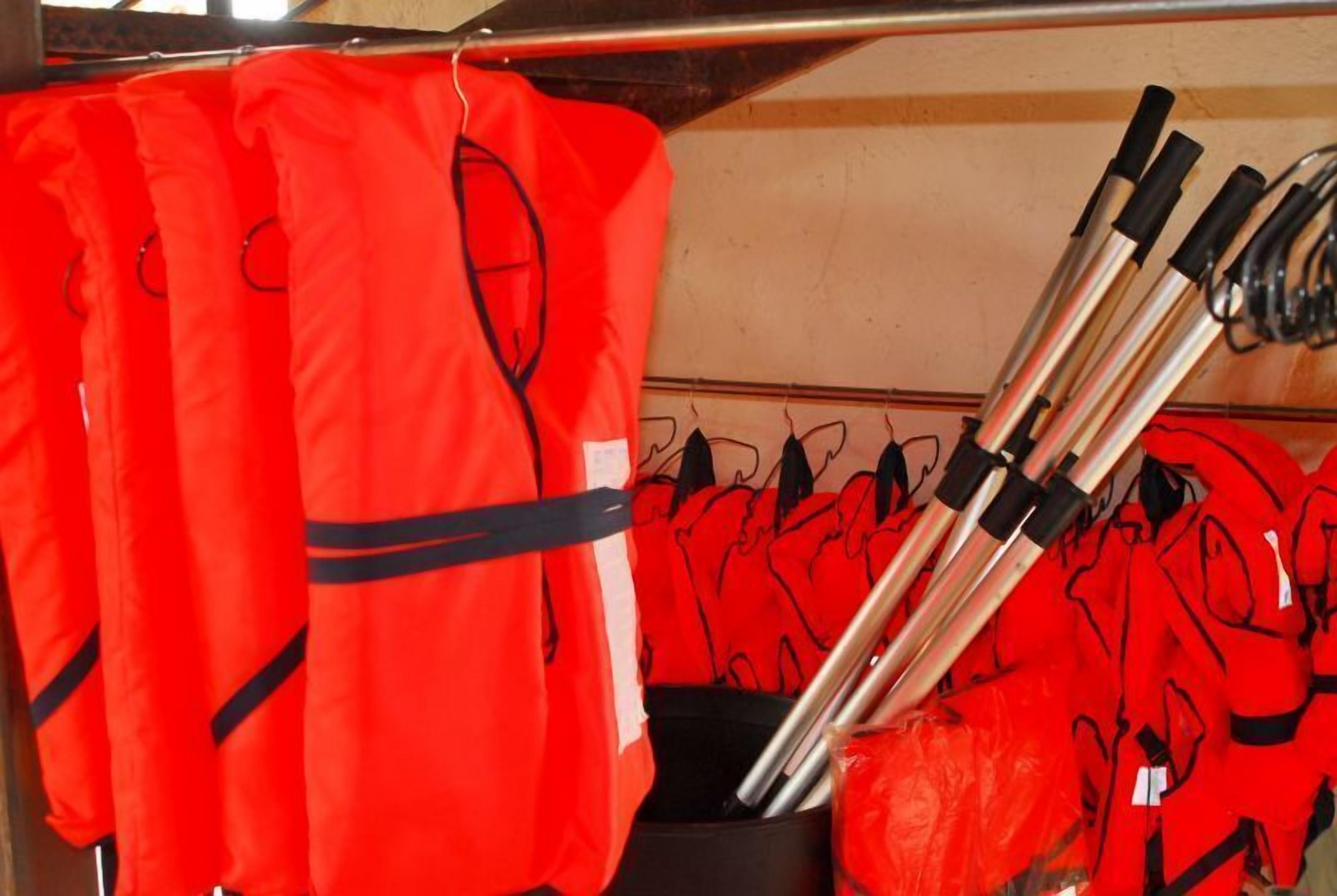 A storage area with red jackets hanging and several metal rods stored in a container.