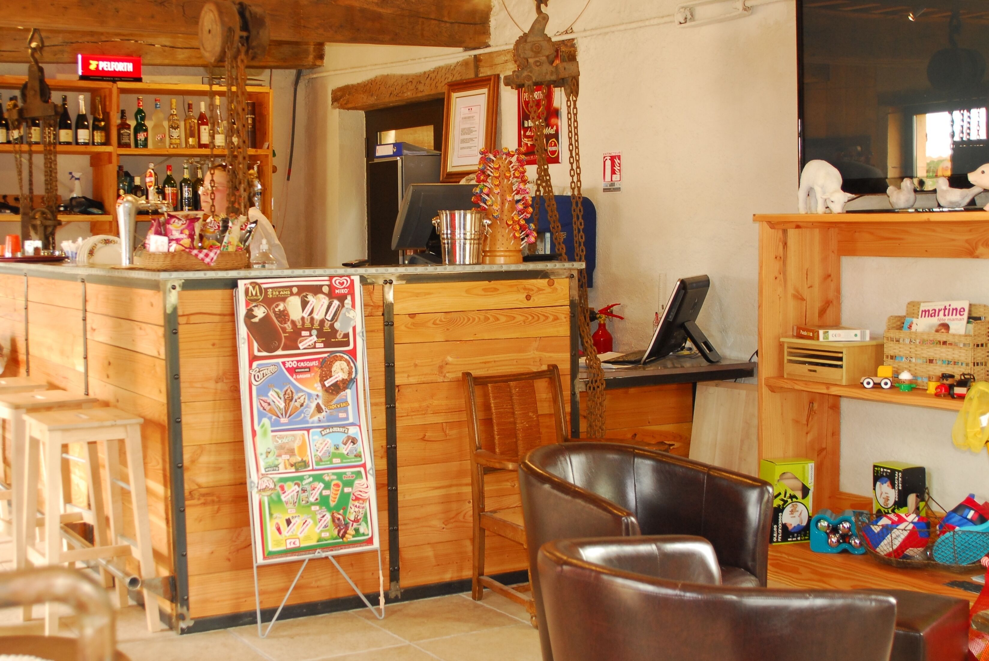 A bar area with wooden shelves, a counter, and a hanging decoration. There are chairs and a wooden table in the foreground.