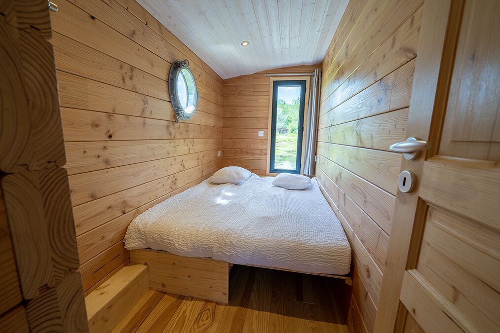 A wooden cabin room with a bed, a window, and a door.