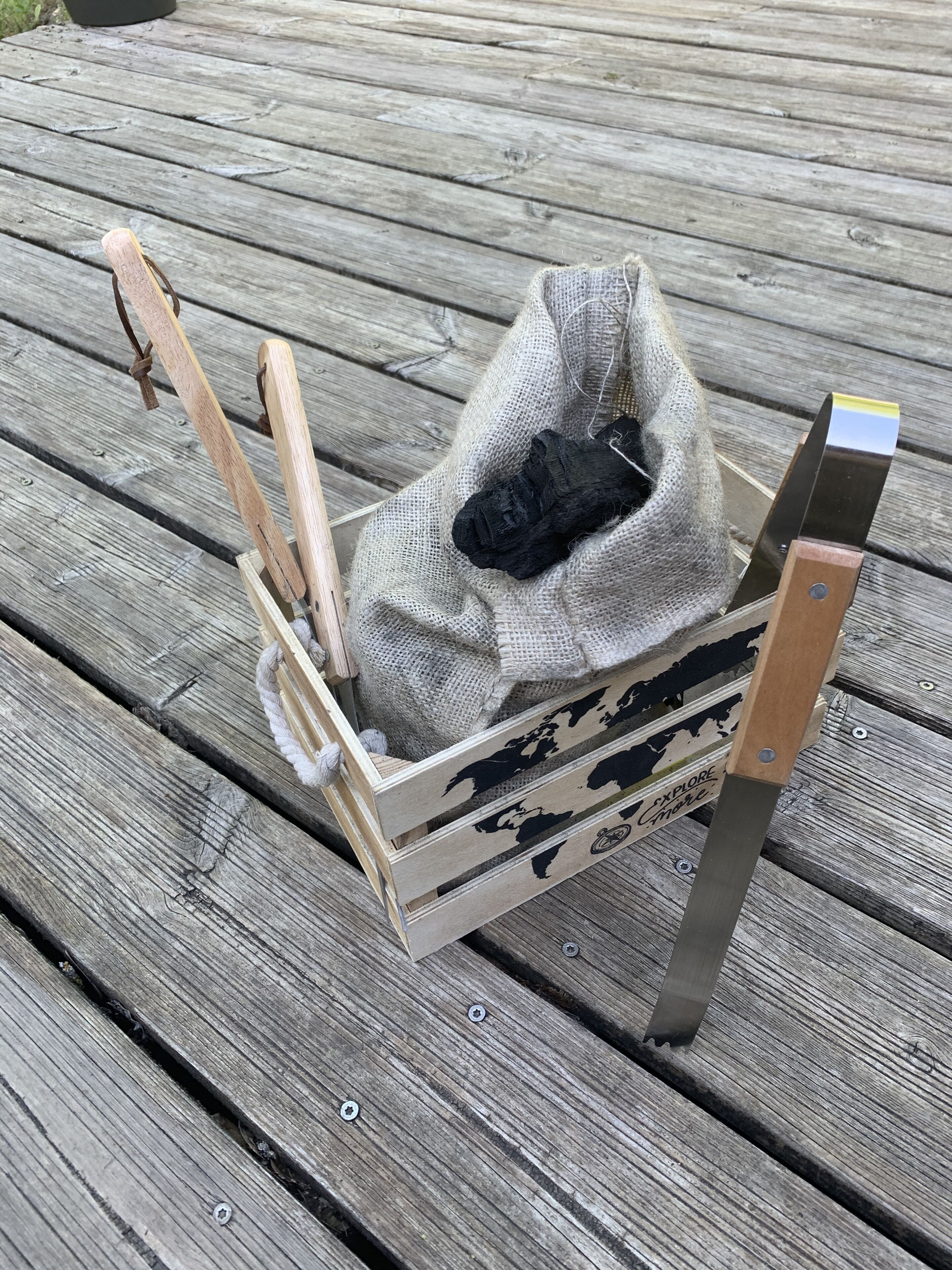 A wooden crate with a world map design, containing a black object and a metal tool, placed on a wooden deck.