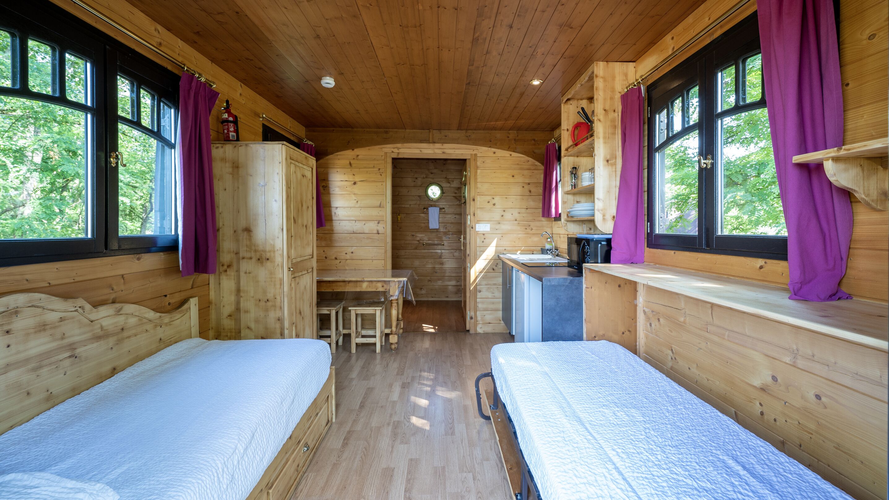 A cabin with two wooden beds, a small kitchenette, and a dining area.