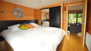 Une chambre aux murs lambrissés, avec un lit, un plafond en bois et une porte donnant sur un balcon.