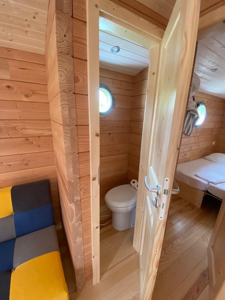 A wooden cabin interior with a small bathroom, a toilet, and a bed.