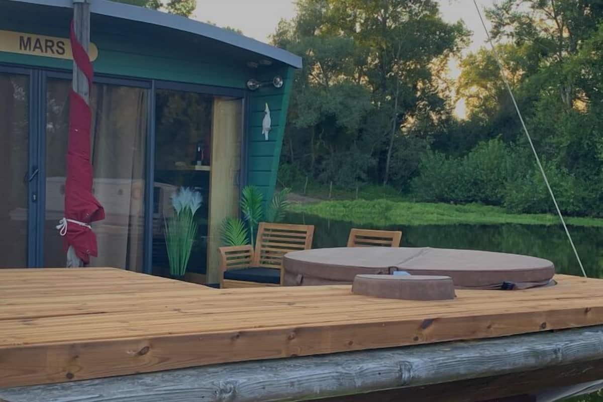 Een houten terras met een tafel en stoelen, een rode parasol en een gebouw met de tekst 'MARS' in de achtergrond.