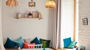 A cozy living room with a white brick wall, a wooden bench with colorful cushions, a white table with a vase, and three hanging lamps. - grätzlhotel Karmelitermarkt (Vienna)