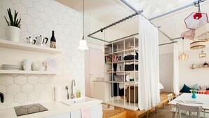 A modern kitchen with a white countertop, a built-in sink, and a hexagonal tile backsplash. There is a wooden staircase leading to a loft area with a white curtain. - grätzlhotel Karmelitermarkt (Vienna)