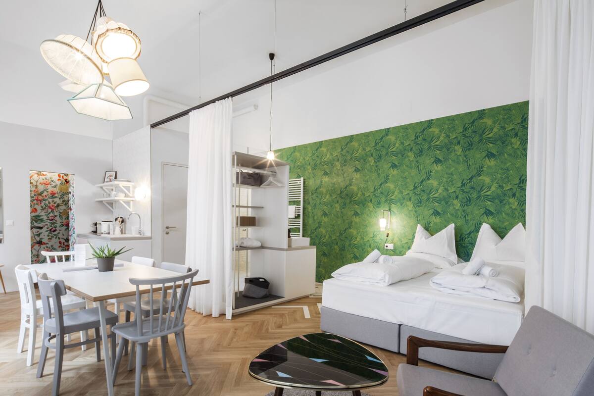 A modern hotel room with a bed, a dining area, and a green leaf-patterned wall.