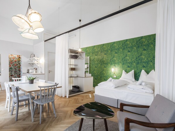 Habitación de hotel moderna con cama, zona de comedor y pared con estampado de hojas verdes.
