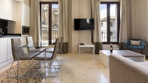 A modern hotel room with a dining area, a sofa, a TV, and a balcony with curtains. - Siloe Plaza (Granada)
