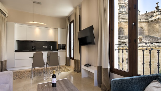 A modern hotel room with a kitchen, dining area, and a balcony with a view of historic architecture. - Siloe Plaza (Granada)