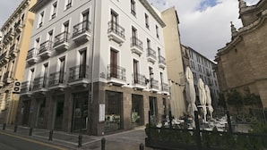 A multi-story building with balconies, storefronts, and outdoor seating. - Siloe Plaza (Granada)