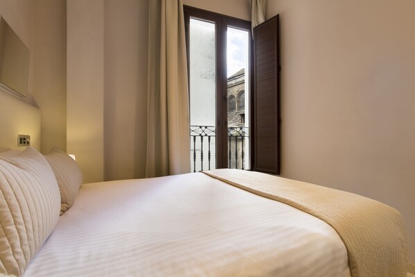 A neatly made bed with a headboard, a window with a view of a building, and a curtain. - Siloe Plaza (Granada)