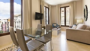 A modern living room with a glass dining table, comfortable seating, a flat-screen TV, and a balcony with a view of buildings. - Siloe Plaza (Granada)