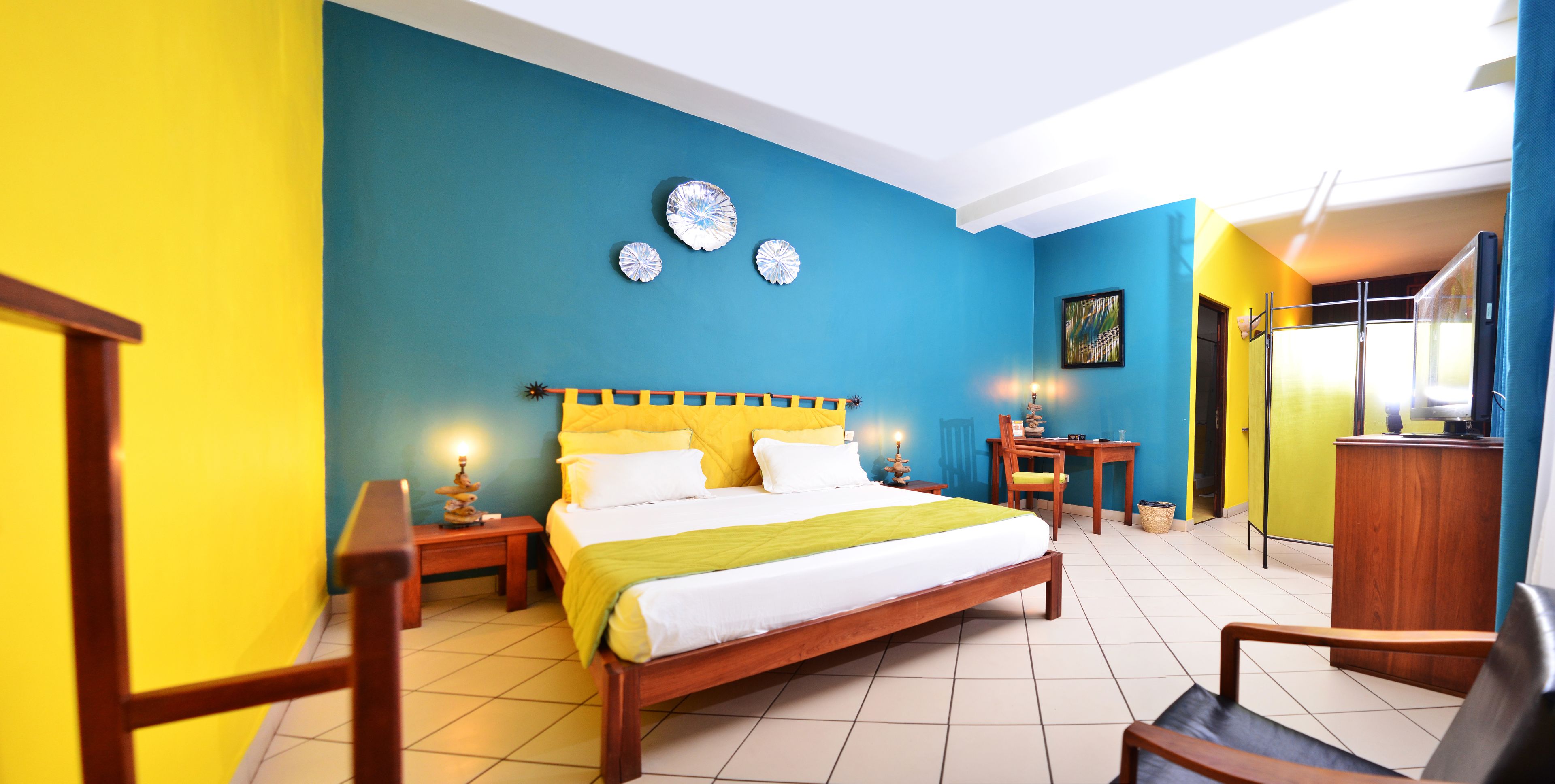 Quarto de hotel com uma cama grande, cabeceira de madeira e uma parede de destaque azul vibrante.