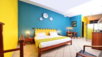 Quarto de hotel com uma cama grande, cabeceira de madeira e uma parede de destaque azul vibrante.