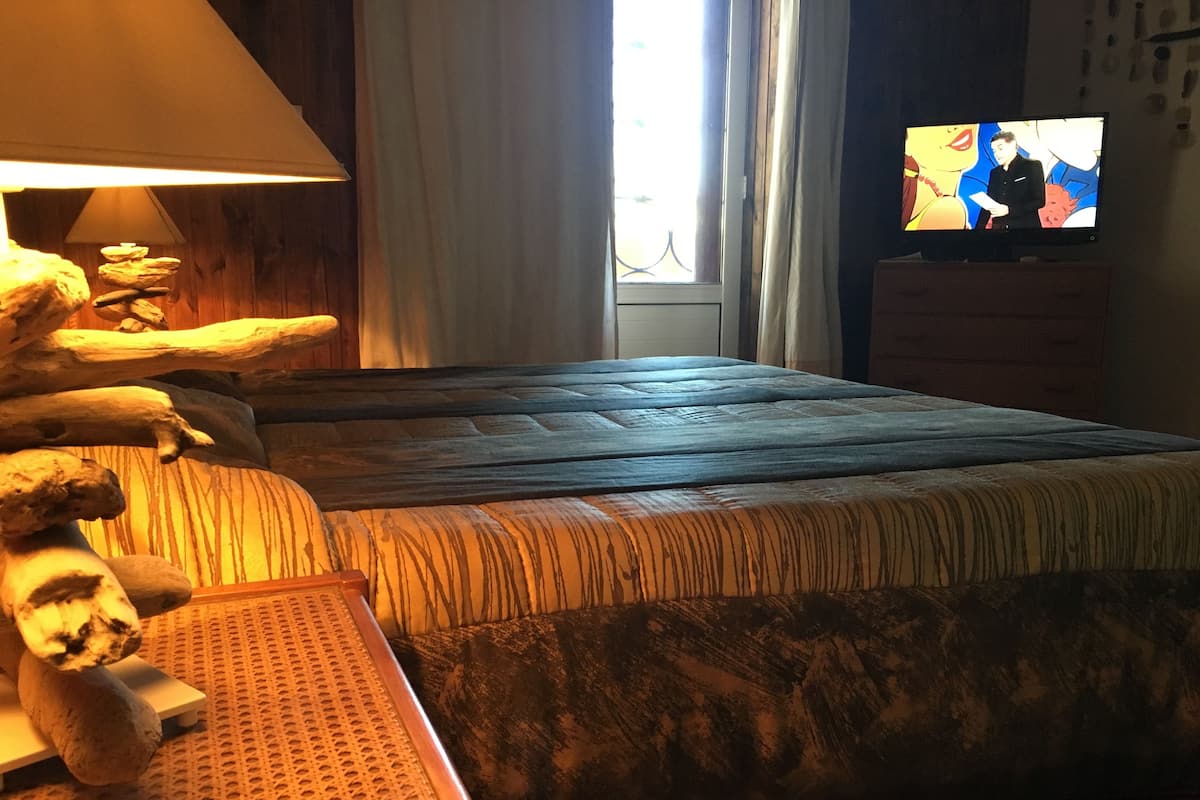 Una habitación con cama, lámpara, televisor y ventana con cortinas.