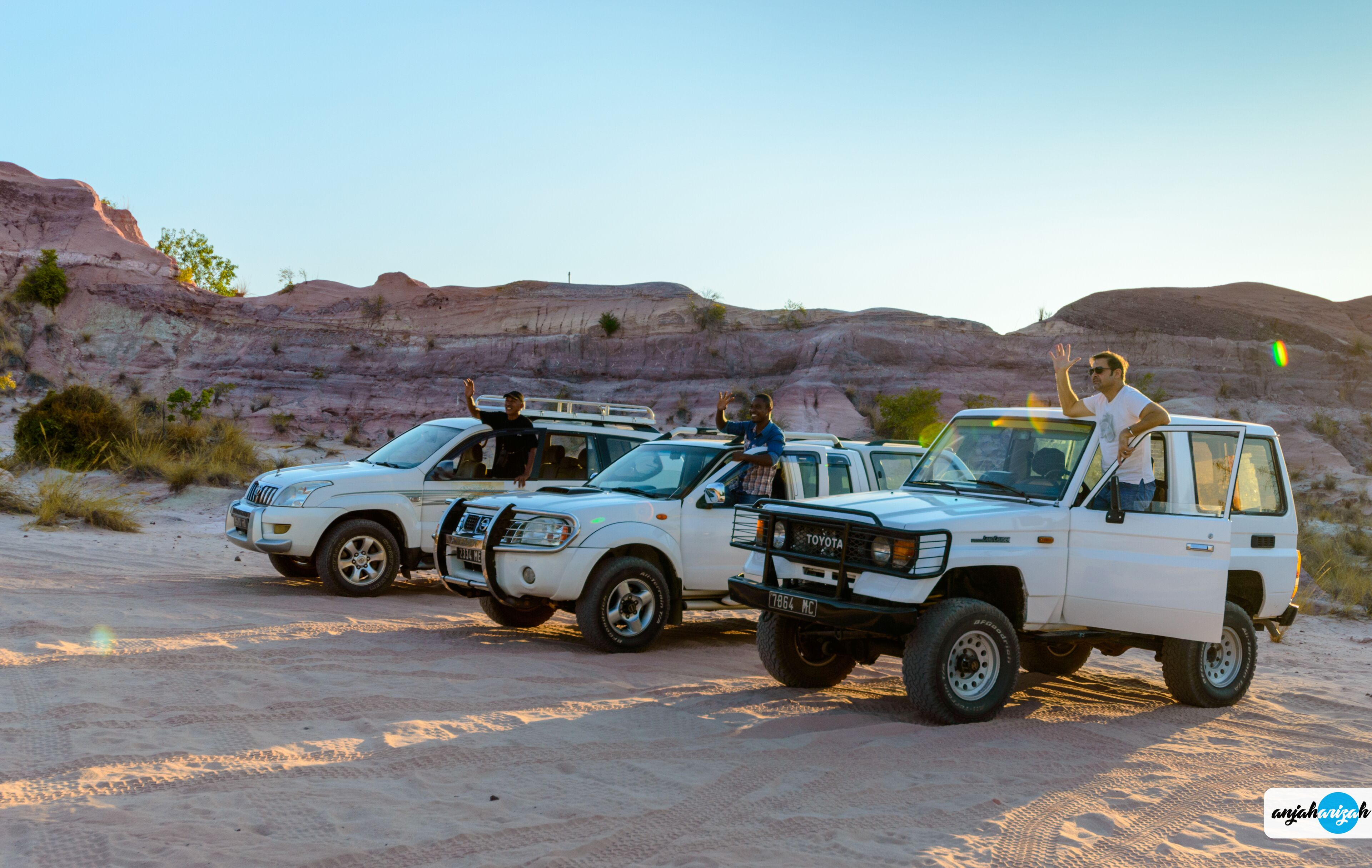 Tres camionetas Toyota blancas estacionadas sobre una superficie arenosa, con un paisaje desértico al fondo.