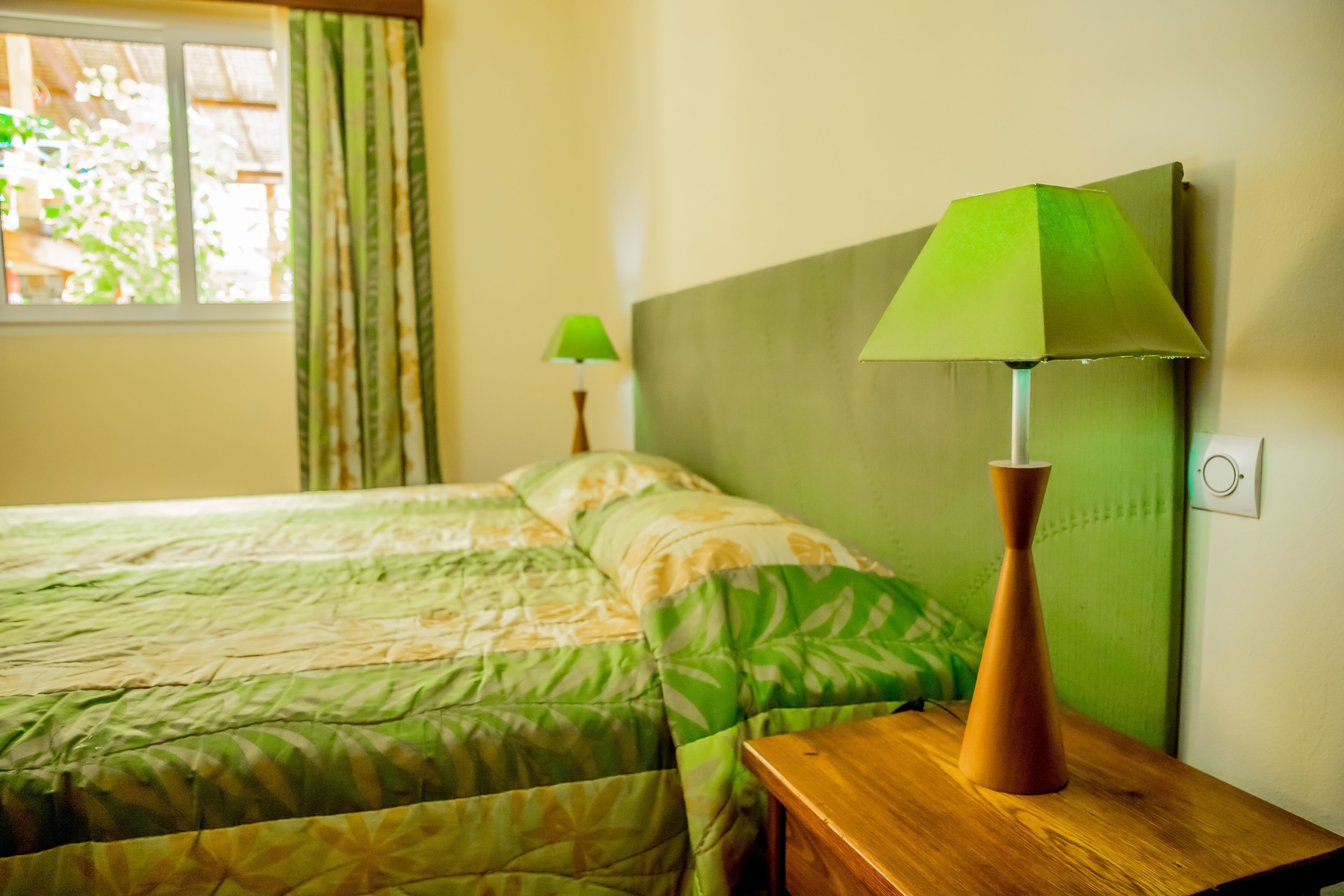 Une chambre d’hôtel avec un lit, une table de chevet, une lampe et une fenêtre avec des rideaux.