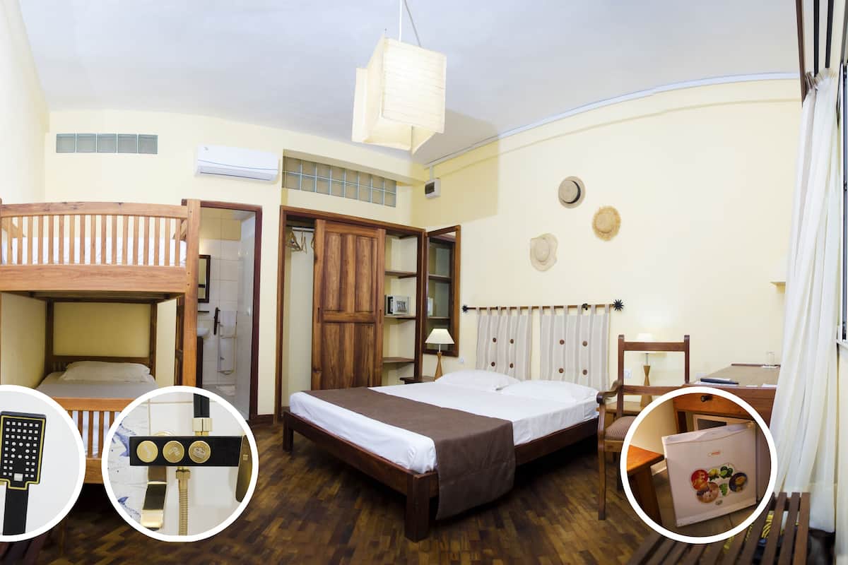 Una habitación con una cama nido, una cama individual, un armario de madera, una mesita con una lámpara y un refrigerador.