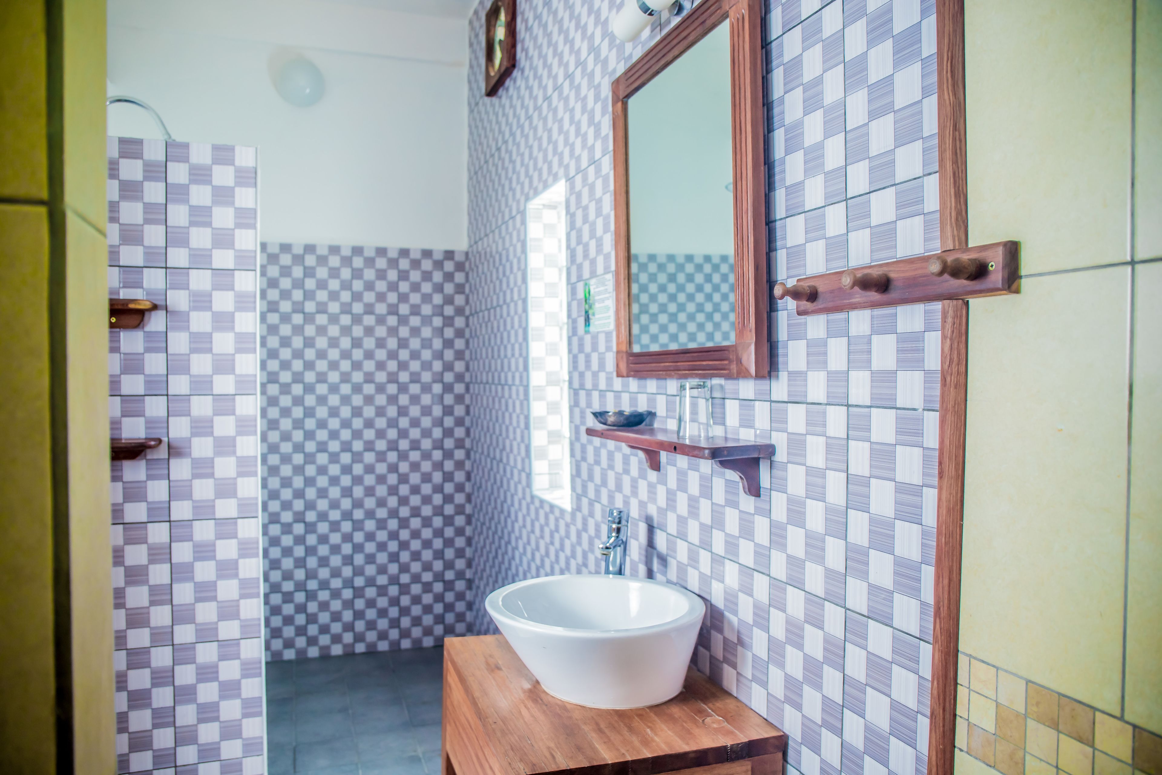 A bathroom with a checkered tile wall, a wooden vanity, a white sink, and a mirror.