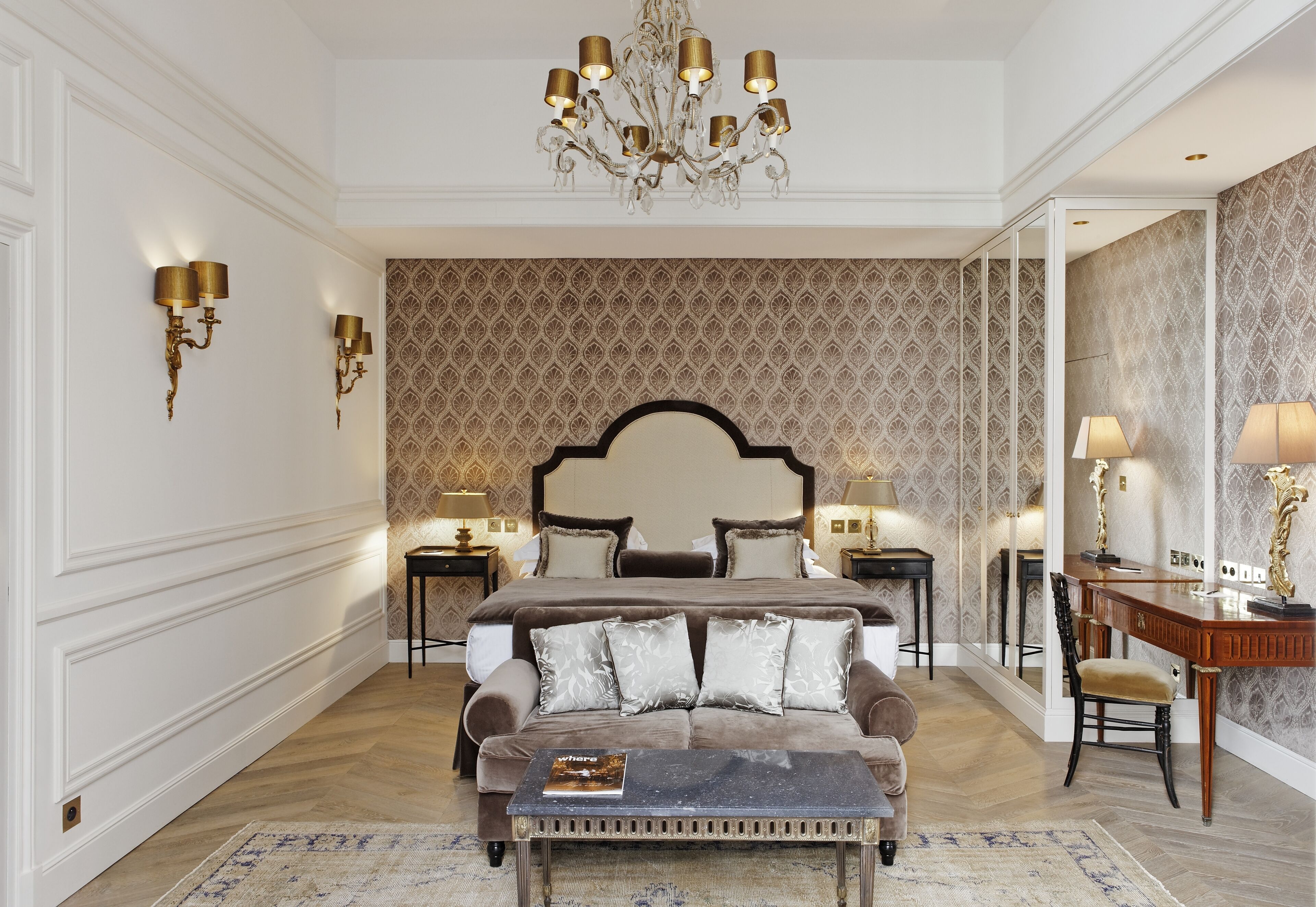 Een slaapkamer met een groot bed, een bank, een bureau en een kroonluchter.