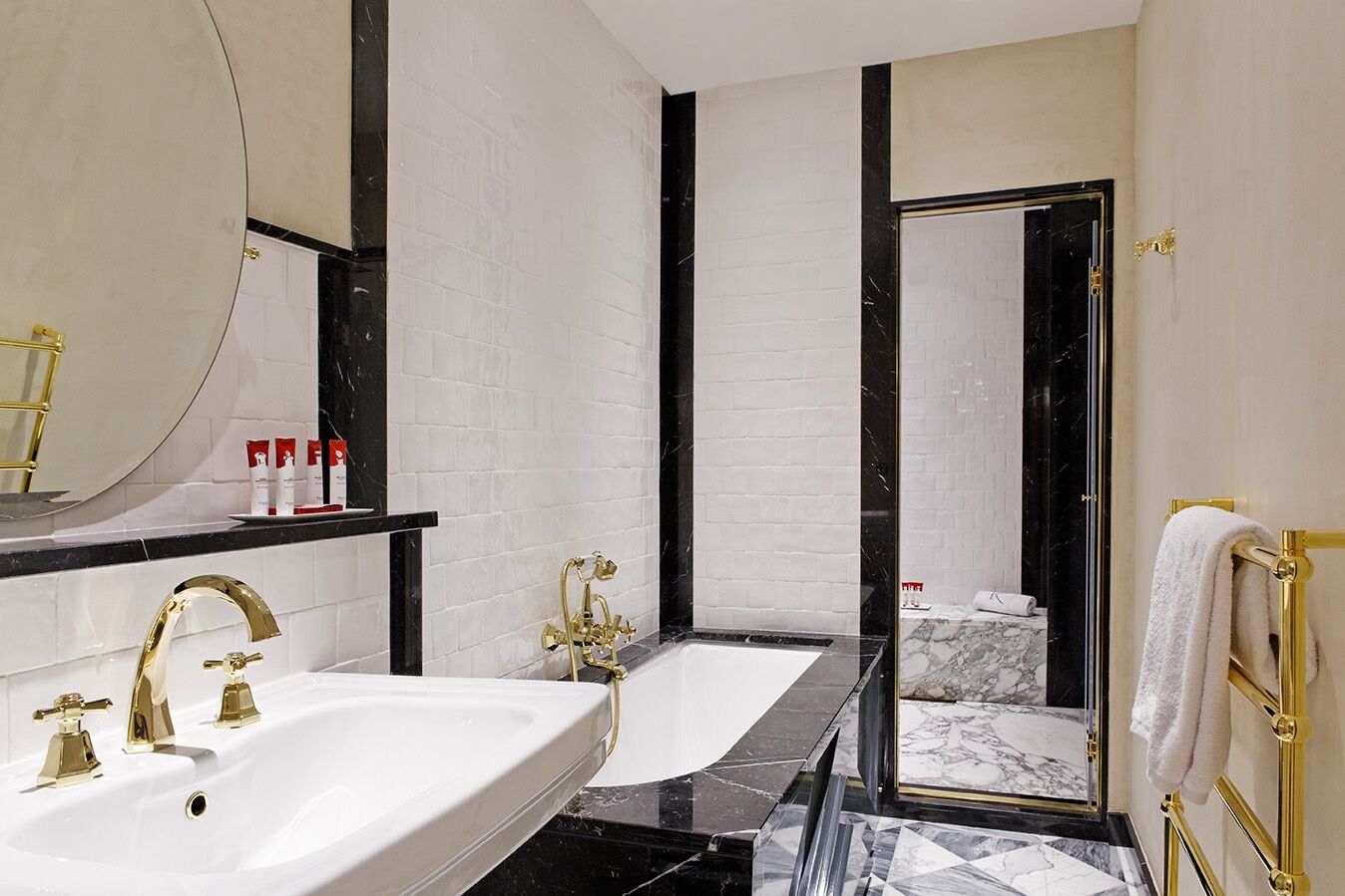 Un baño moderno con un lavamanos grande blanco, grifos dorados, una bañera de mármol negro y una ducha con cerramiento de vidrio.