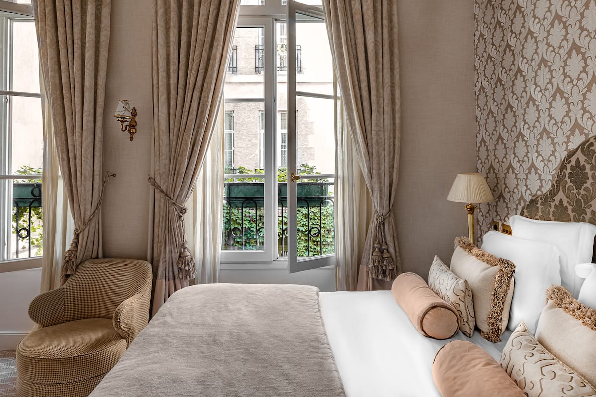 Un dormitorio con una cama grande, una silla y vistas a un balcón con vegetación.