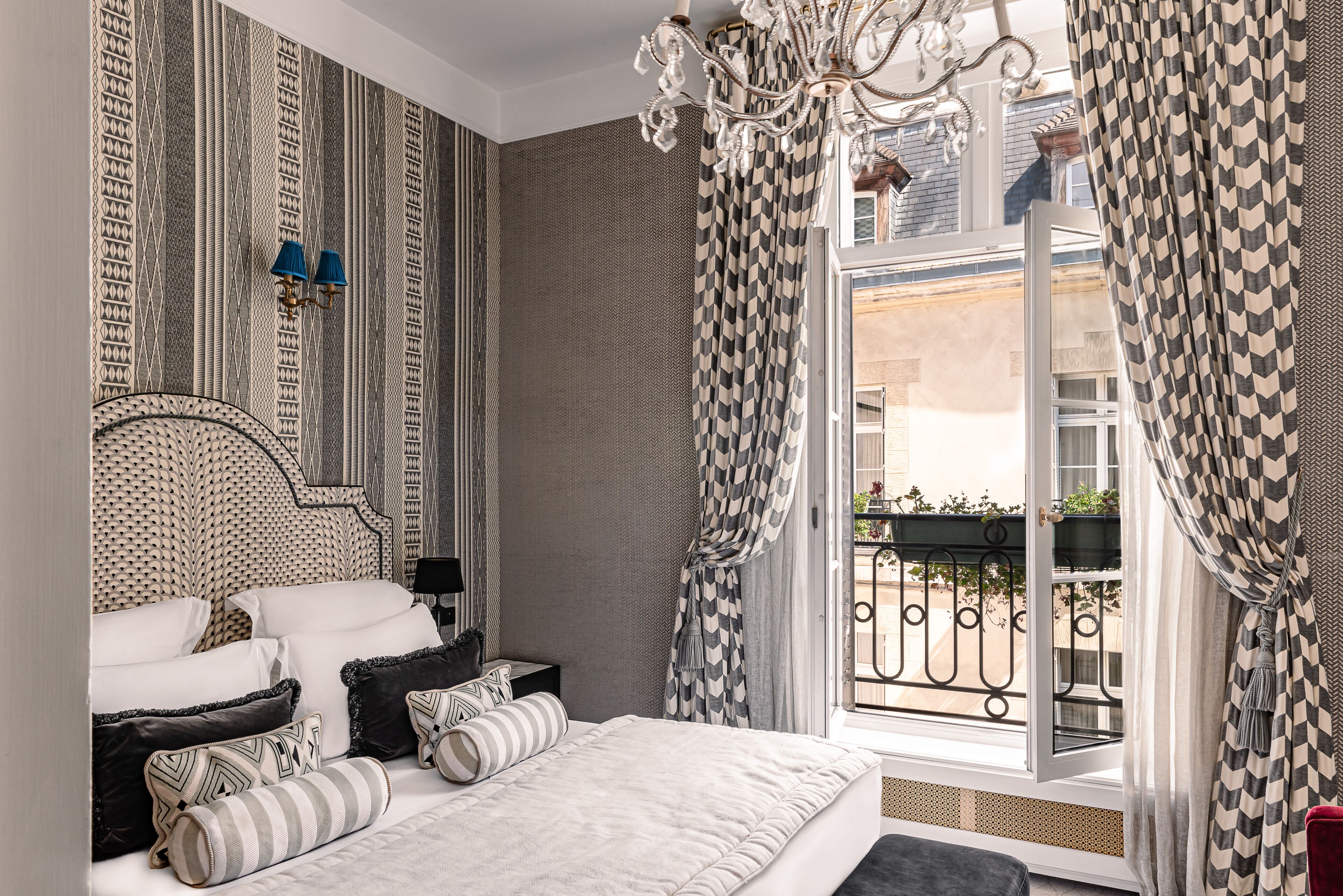 Ein Schlafzimmer mit einem Bett, Nachttischen, einem Chandelier und einem Fenster mit gemusterten Vorhängen.