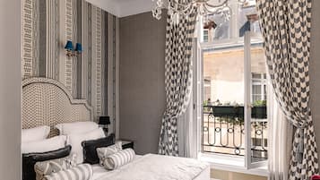 Ein Schlafzimmer mit einem Bett, Nachttischen, einem Chandelier und einem Fenster mit gemusterten Vorhängen.