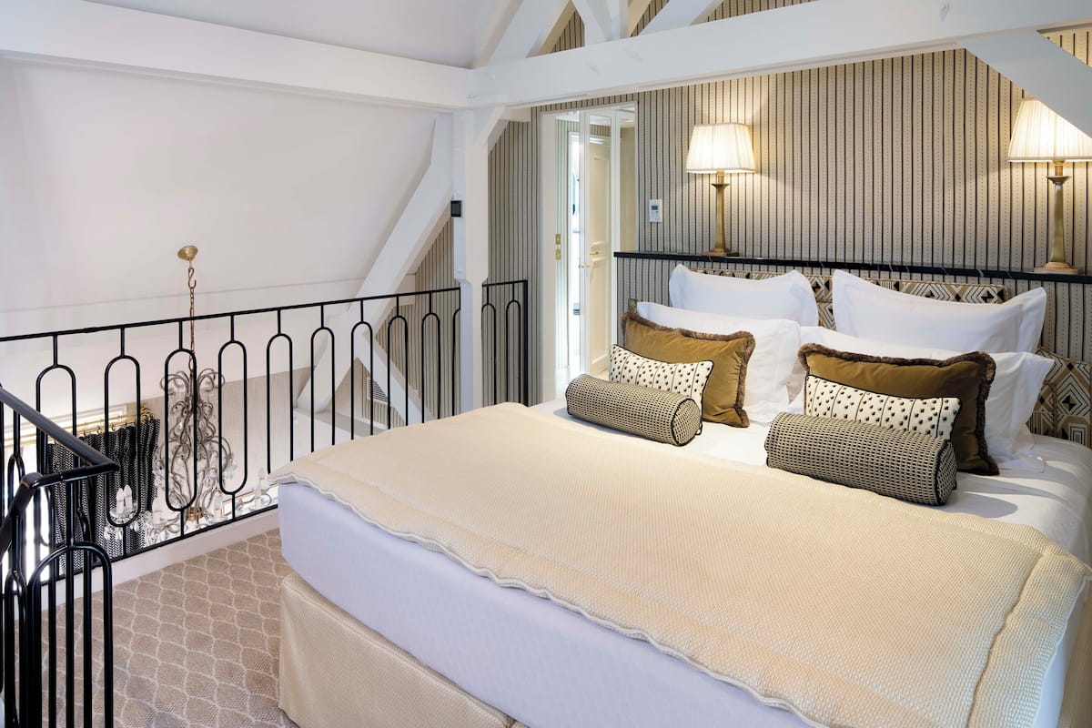 Un dormitorio con cama, almohadas, cabecera, barandilla y pared con diseño a rayas.
