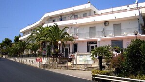 Un hotel de dos pisos con balcones, fachada de piedra y palmeras en primer plano.